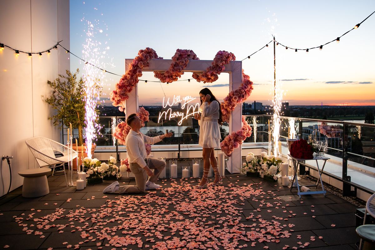 Heiratsantrag auf Rooftop in Düsseldorf mit rosa Blumenherz bei Sonnenuntergang